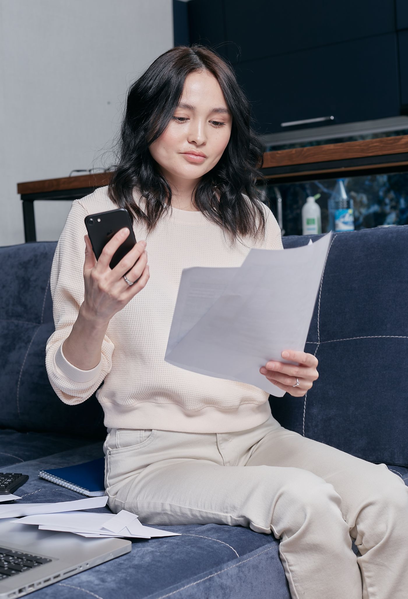 Woman on a couch checking a bill against her phone